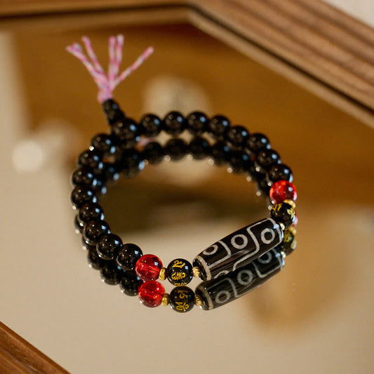 Tibetan Nine-Eye Dzi Bead Black Onyx Bracelet – angled shot on wood showing dzi focal & tassel, protection jewelry