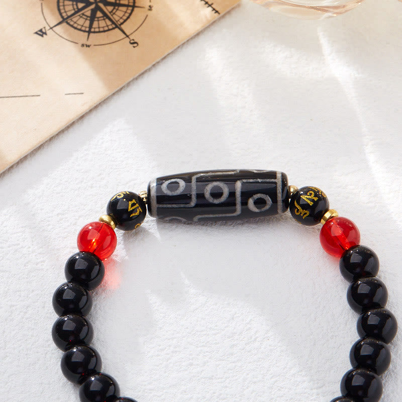 Tibetan Nine-Eye Dzi Bead Black Onyx Bracelet – close-up on soft white fabric, dzi center & tassel, healing bracelet