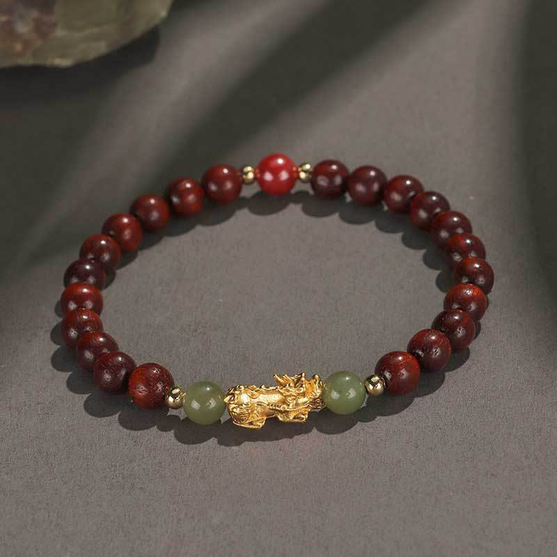 Multi-Wood PiXiu Bracelet – Deep red wood bracelet with gold PiXiu, green jade and red bead on gray surface