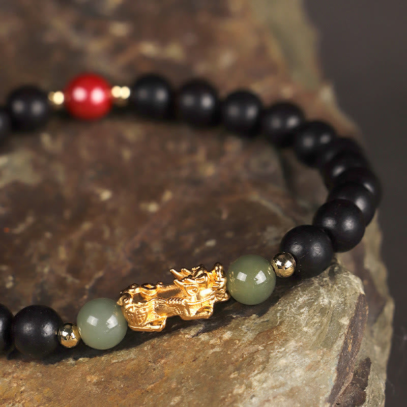 Multi-Wood PiXiu Bracelet – Close-up of black ebony bracelet with gold PiXiu and green jade on natural rock