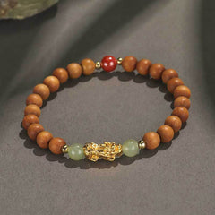 Multi-Wood PiXiu Bracelet – Light brown wood beads with gold PiXiu, green jade and red cinnabar on gray surface