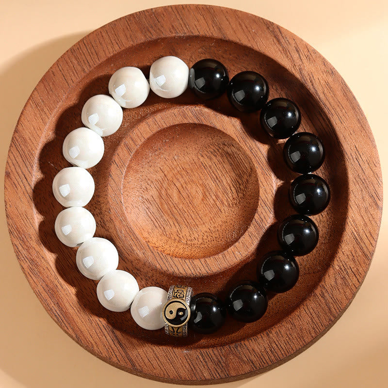 Black Obsidian White Porcelain Yin Yang Bracelet - Circular yin-yang bracelet on wooden dish top-down view, feng shui jewelry