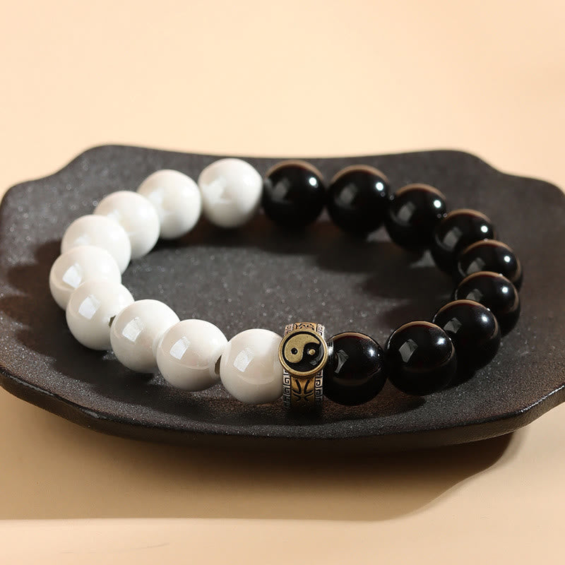 Black Obsidian White Porcelain Yin Yang Bracelet - Circular yin-yang bracelet on dark dish with lotus charm, spiritual balance jewelry