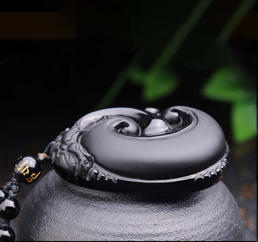 Black Obsidian PiXiu Pendant – Side view of obsidian pendant on black stone with green leaf