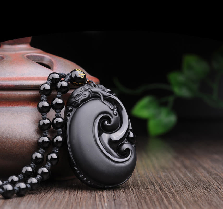 Black Obsidian PiXiu Pendant – Obsidian swirl pendant with beads leaning on clay pottery