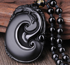 Black Obsidian PiXiu Pendant – Close-up of carved swirl obsidian with bead chain on wood