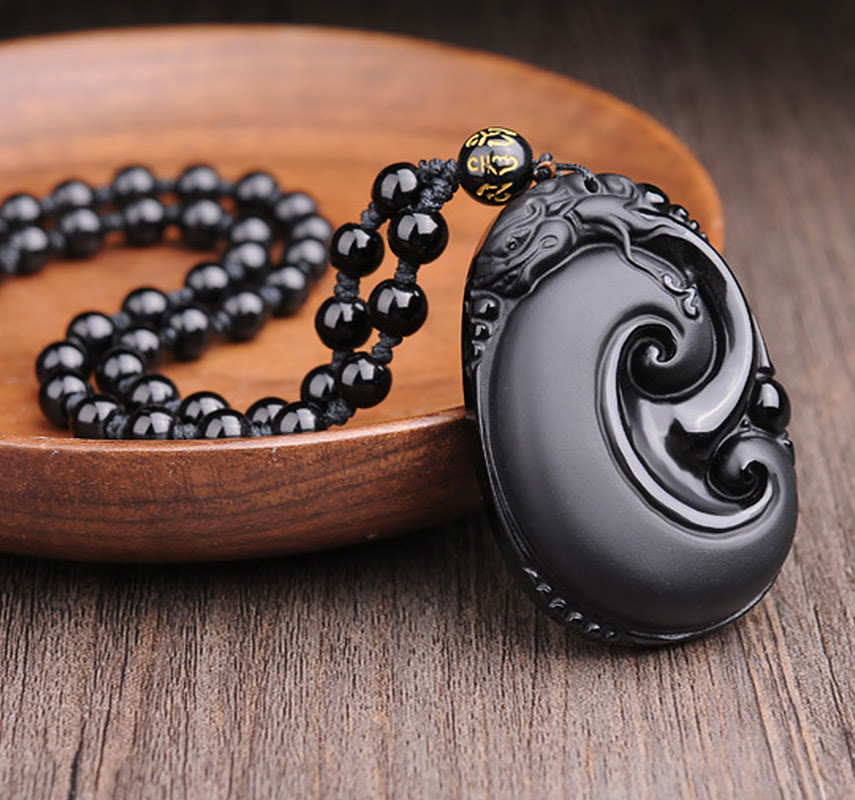 Black Obsidian PiXiu Pendant – Oval obsidian swirl pendant with black bead necklace on wood