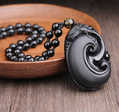 Black Obsidian PiXiu Pendant – Oval obsidian swirl pendant with black bead necklace on wood