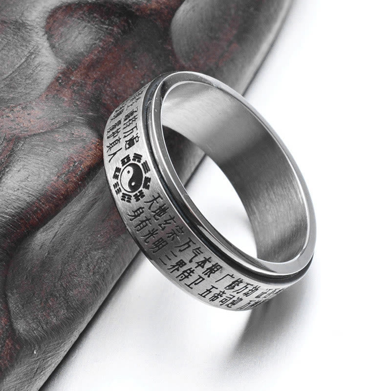 Bagua Yin Yang Titanium Steel Rotatable Ring - silver ring with gold Taoist text and yin-yang on dark stone surface, medit...