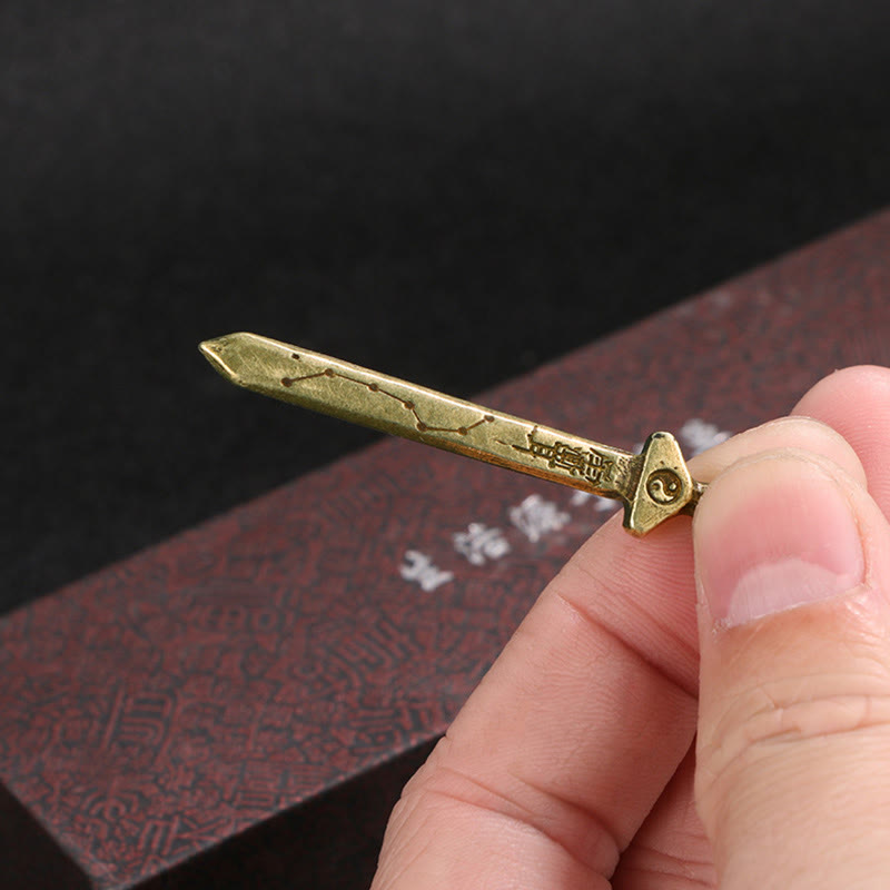 Vintage Yin Yang Copper Sword Necklace - miniature brass sword pendant held in hand, showing yin-yang symbol and constella...
