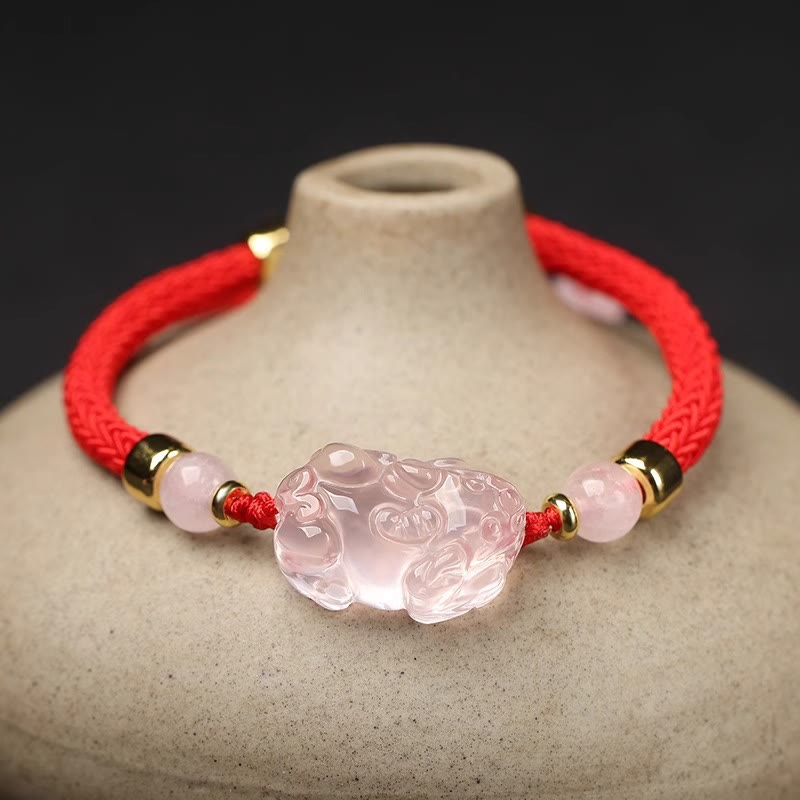 Pink Crystal PiXiu Bracelet – Pink crystal PiXiu on red cord draped over beige pottery vase