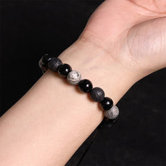 Black Obsidian Lava Rock Yin Yang Bracelet - worn on wrist close-up, solid black background, three-bead pattern