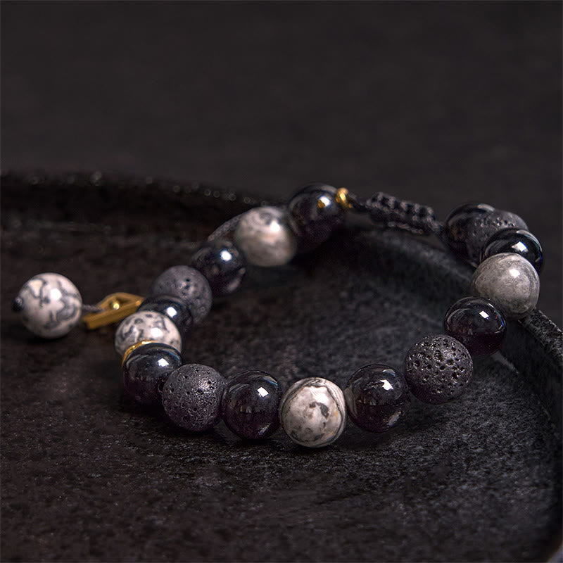 Black Obsidian Lava Rock Yin Yang Bracelet - low angle on dark stone in shallow bowl, blue silk accent, gold details