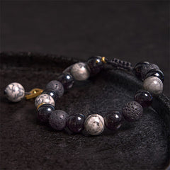 Black Obsidian Lava Rock Yin Yang Bracelet - low angle on dark stone in shallow bowl, blue silk accent, gold details