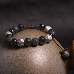Black Obsidian Lava Rock Yin Yang Bracelet - draped on ceramic prop, moody dark background, natural stone beads