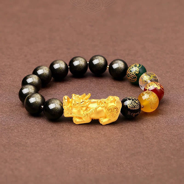 Obsidian PiXiu Five Gods Bracelet – Flat lay on brown fabric with black obsidian, gold PiXiu and five gods beads, wealth