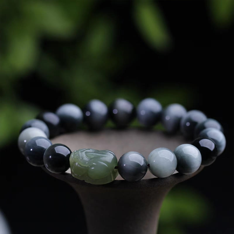 Eagle's Eye Jade PiXiu Bracelet – dark gray eagle eye stone beads with green jade PiXiu on stand, nature backdrop