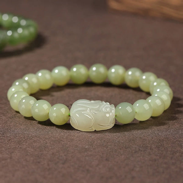 Hetian Jade PiXiu Bracelet – light green jade beads with carved PiXiu on brown fabric, front view, fortune jewelry