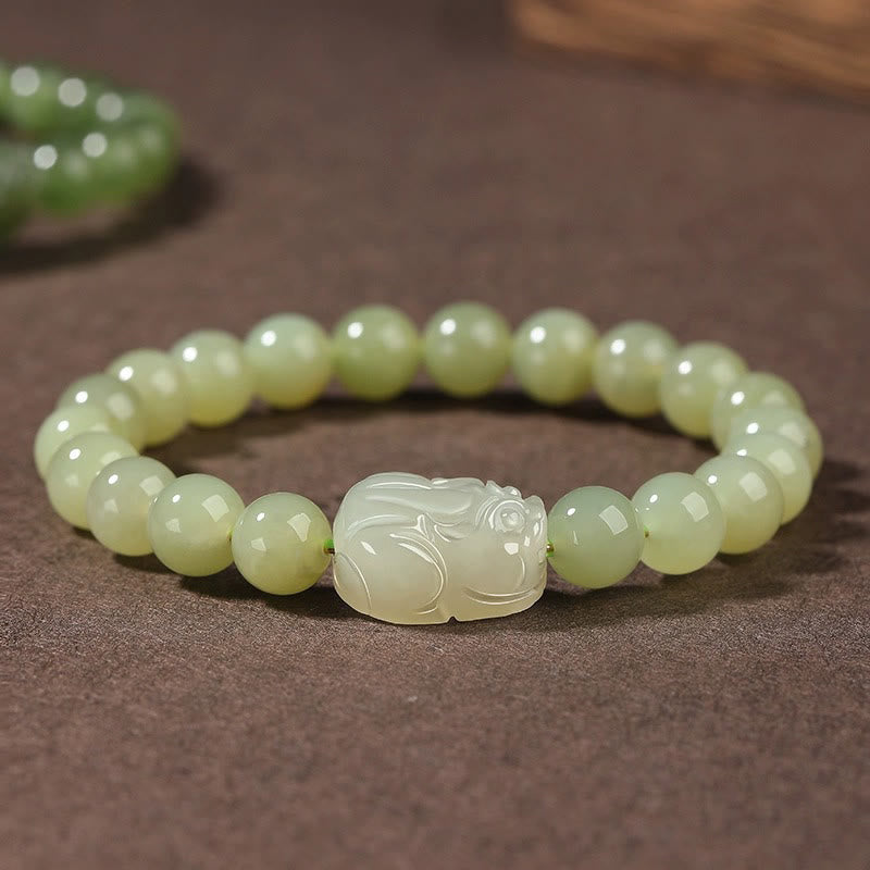 Hetian Jade PiXiu Bracelet – light green jade beads with carved PiXiu on brown fabric, front view, fortune jewelry