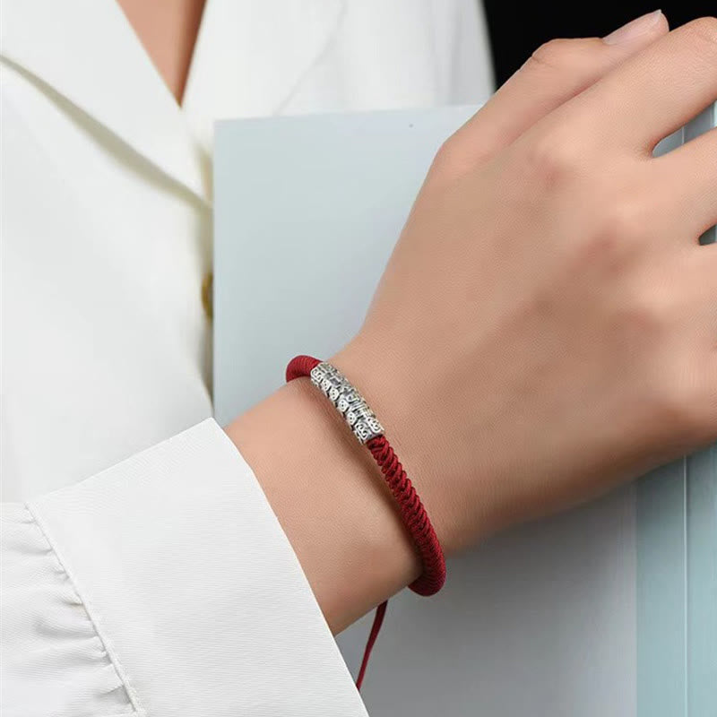 Silver Mantra Rope Bracelet – Red cord bracelet with silver charm on wrist over blue-gray surface, blessing bracelet