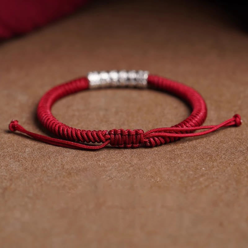 Silver Mantra Rope Bracelet – Adjustable red cord bracelet with silver barrel bead on brown surface, knot closure