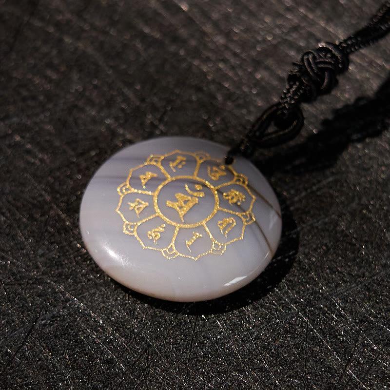 Om Mani Padme Hum Necklace – Banded agate at oblique angle on dark woven fabric, gold Sanskrit crystal