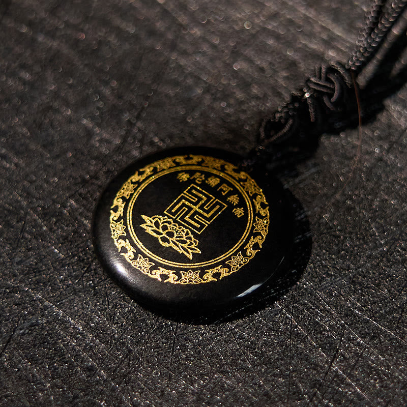Black Obsidian Purification Pendant - elevated close-up, gold Namo Amitabha mantra & lotus on obsidian, moody dark texture