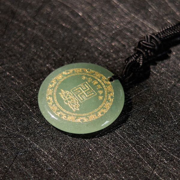 Green Jade Purification Pendant - olive jade with gold mantra border, on pebbled dark leather, warm chiaroscuro