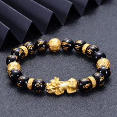 Black Obsidian PiXiu Om Mani Padme Hum Bracelet – on dark textured surface with black ribbon, angled view, spiritual jewelry