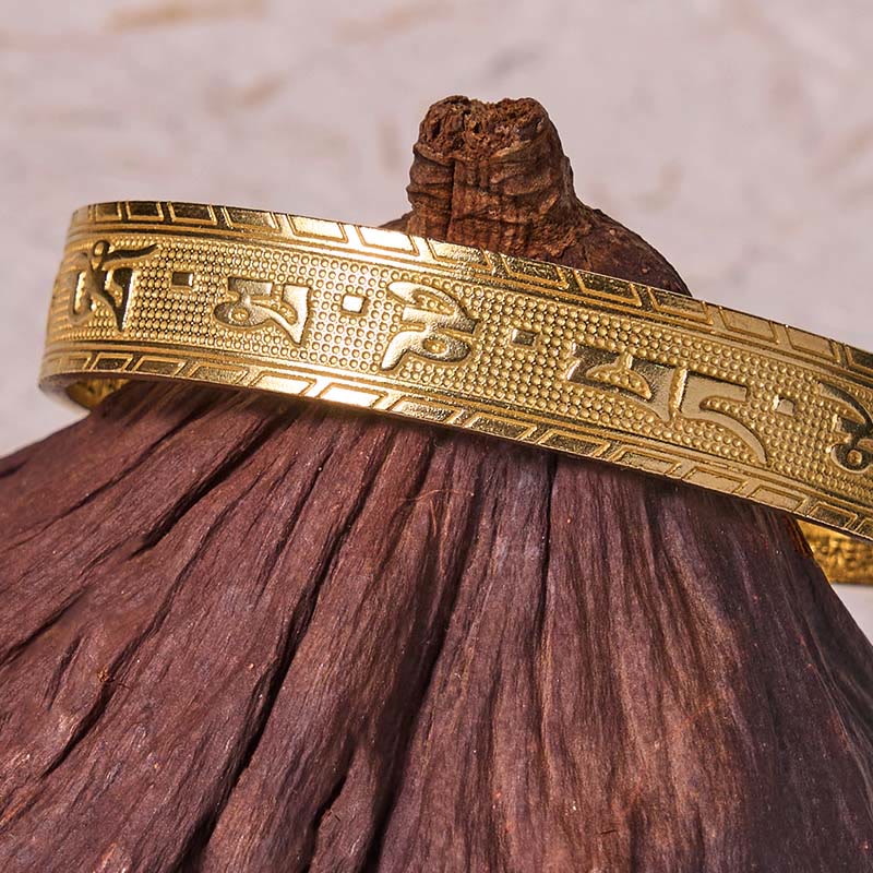 Om Mani Padme Hum Copper Brass Bangle – Close-up on dark wood, embossed border detail
