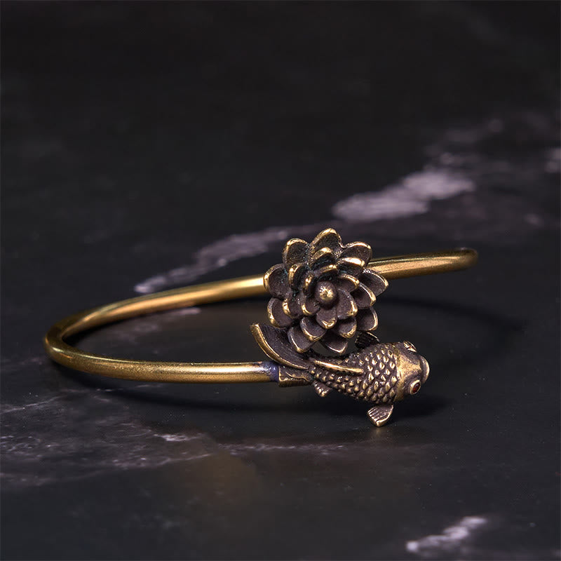 Lotus Koi Fish Copper Brass Luck Bangle – open cuff with sculpted lotus and koi with red eye, 45 angle on dark stone