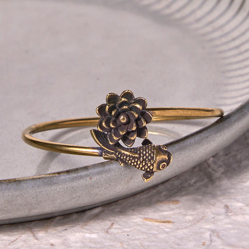 Lotus Koi Fish Copper Brass Luck Bangle – adjustable cuff on gray ceramic dish, lotus above koi below with red eye