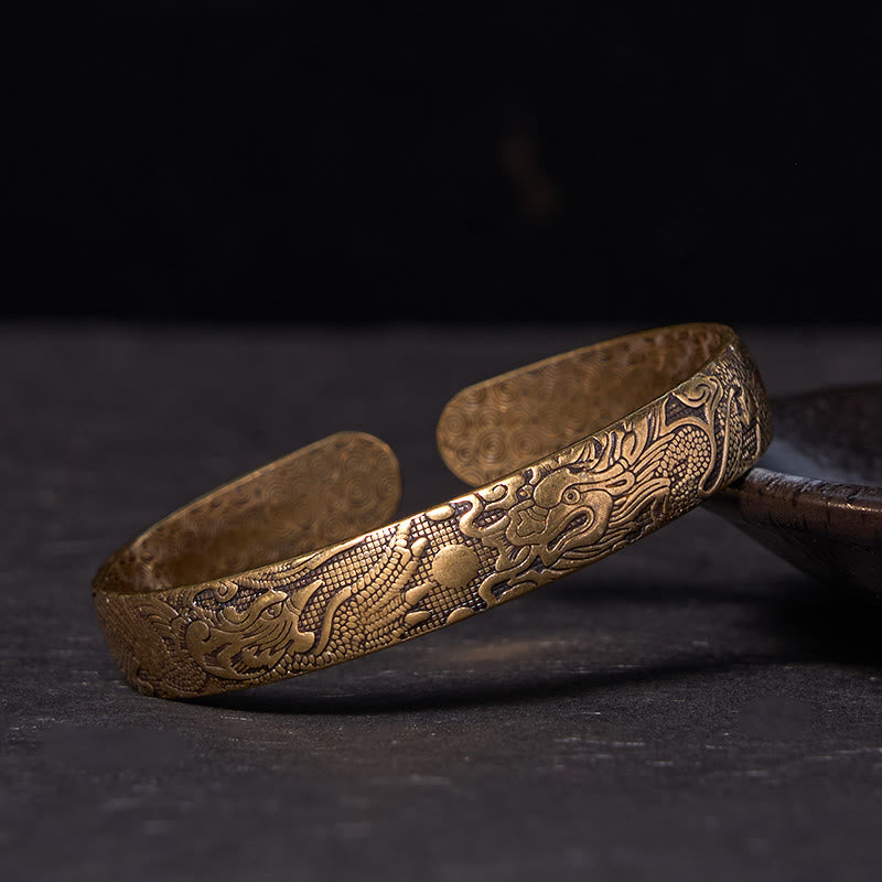 Dragon Phoenix Copper Brass Bracelet – Three-quarter view on dark stone, engraved dragon and phoenix relief, Protective