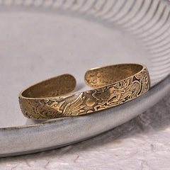 Dragon Phoenix Copper Brass Bracelet – Resting on gray ceramic plate, detailed dragon-phoenix motifs, Artisan