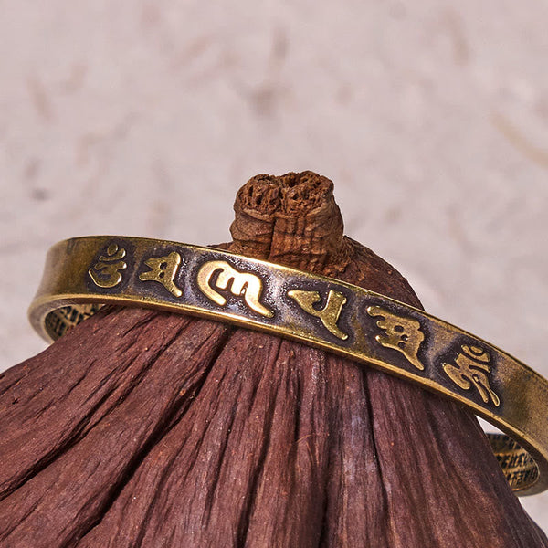 Om Mani Padme Hum Copper Cuff Bangle – Resting on natural wood, gold-toned relief script, artisan jewelry