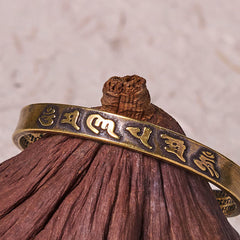 Om Mani Padme Hum Copper Cuff Bangle – Resting on natural wood, gold-toned relief script, artisan jewelry