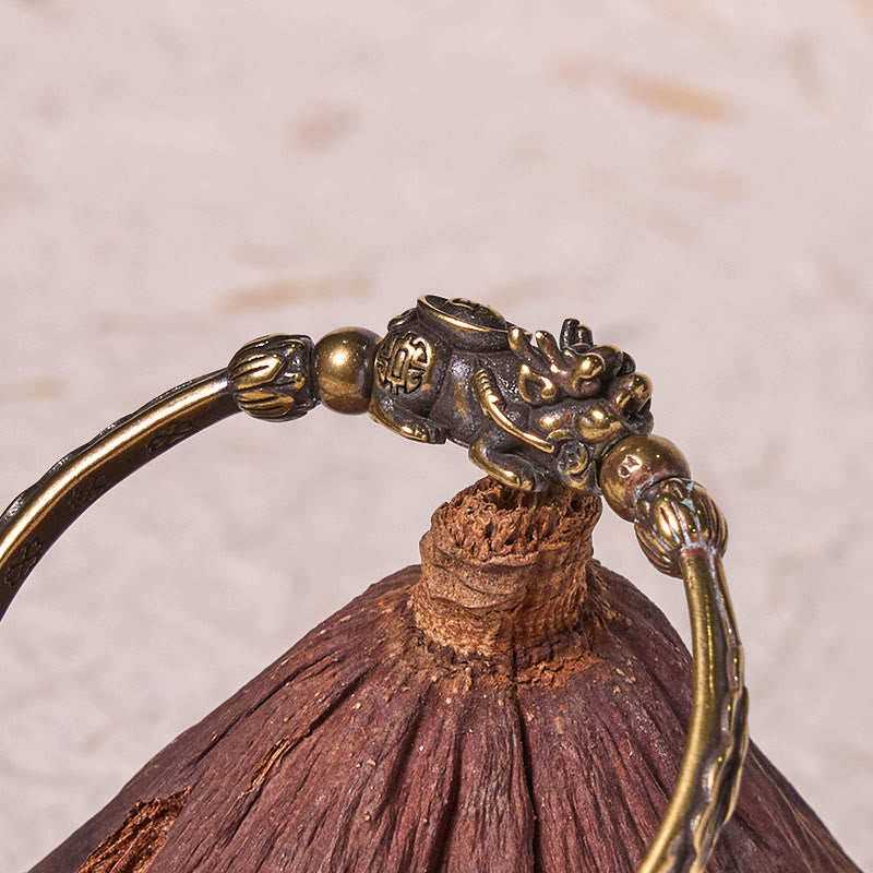 PiXiu Coin Bangle – Close-up of PiXiu lotus detail on brass cuff over wood texture