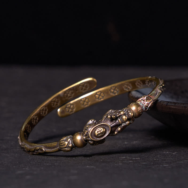 PiXiu Coin Bangle – Side view of PiXiu coin brass cuff resting on dark wooden plate