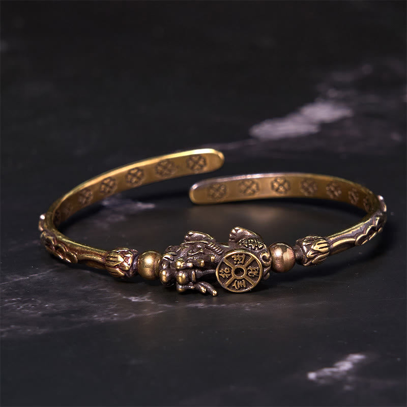 PiXiu Coin Bangle – Brass open cuff with PiXiu holding coin on black marble background