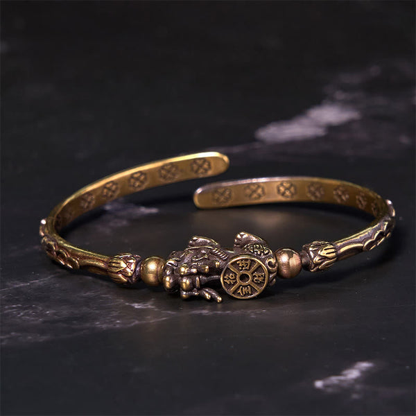 PiXiu Coin Bangle – Brass open cuff with PiXiu holding coin on black marble background