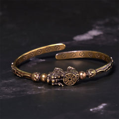 PiXiu Coin Bangle – Brass open cuff with PiXiu holding coin on black marble background