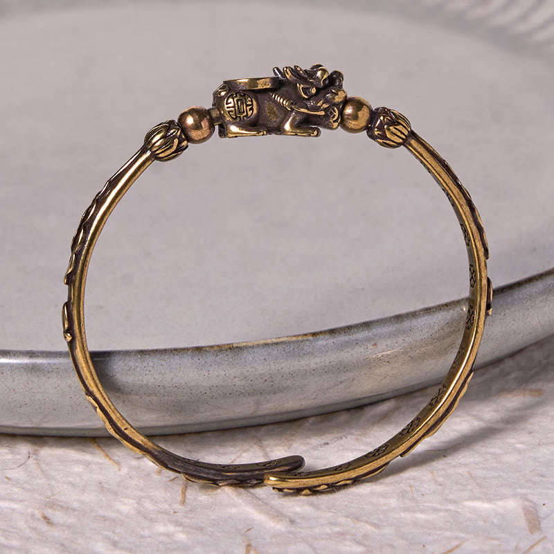 PiXiu Coin Bangle – Brass cuff with PiXiu coin detail on gray ceramic dish