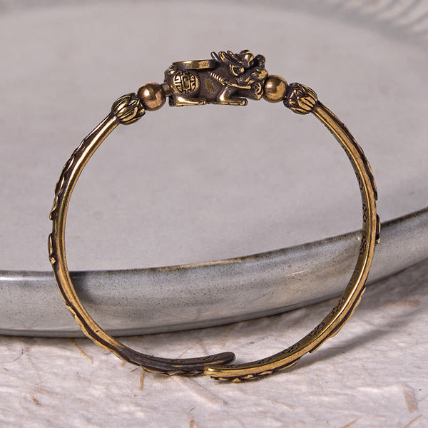 PiXiu Coin Bangle – Brass cuff with PiXiu coin detail on gray ceramic dish