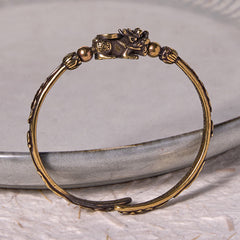 PiXiu Coin Bangle – Brass cuff with PiXiu coin detail on gray ceramic dish