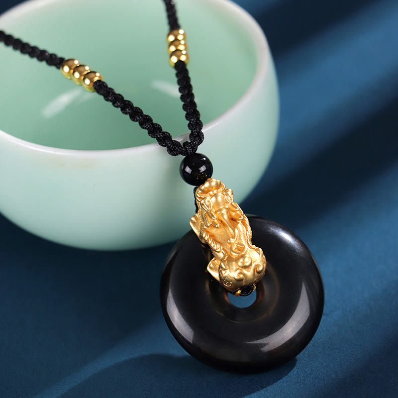 Black Onyx Agate Peace Buckle PiXiu Necklace – close-up black onyx peace buckle with gold PiXiu on cord, teal cup background