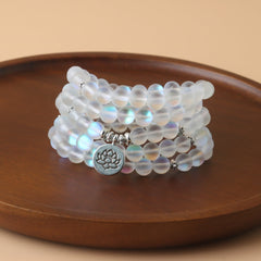 108 Mala Glitter Stone Lotus Bracelet – iridescent beads with silver lotus charm on wood dish, focused