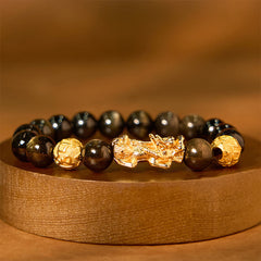 Gold Sheen Obsidian PiXiu Bracelet – Black golden-sheen beads with gold PiXiu on wood stand, wealth jewelry