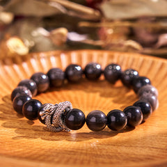 Silver Sheen Obsidian Dragon Bracelet – full bracelet on fluted wooden plate with bokeh background, mystical aura