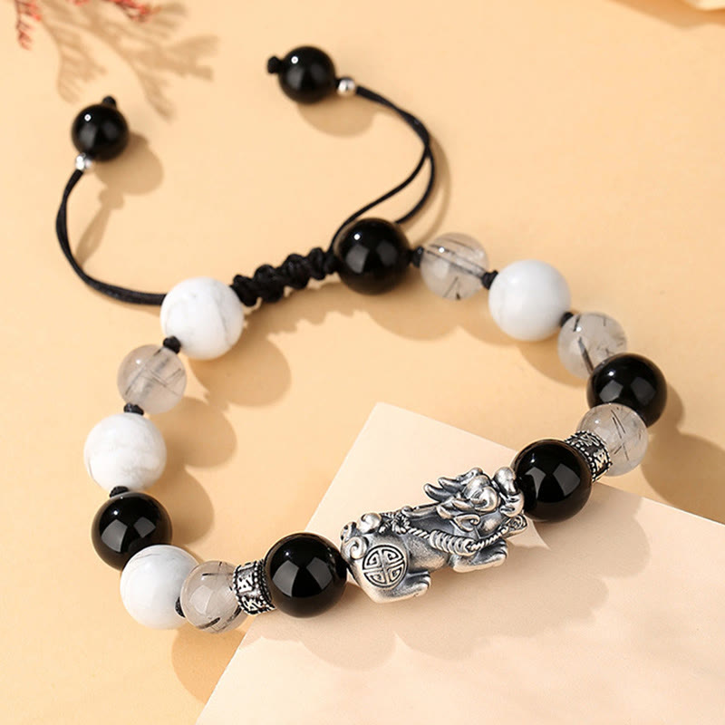 Black Obsidian Pi Xiu Bracelet – Angled flat lay on beige paper, black cord knot detail, sterling silver Pi Xiu centerpiece
