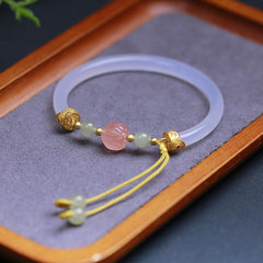White Agate Lotus Hetian Jade Bracelet – translucent bangle with pink lotus bead on wood tray, mindful